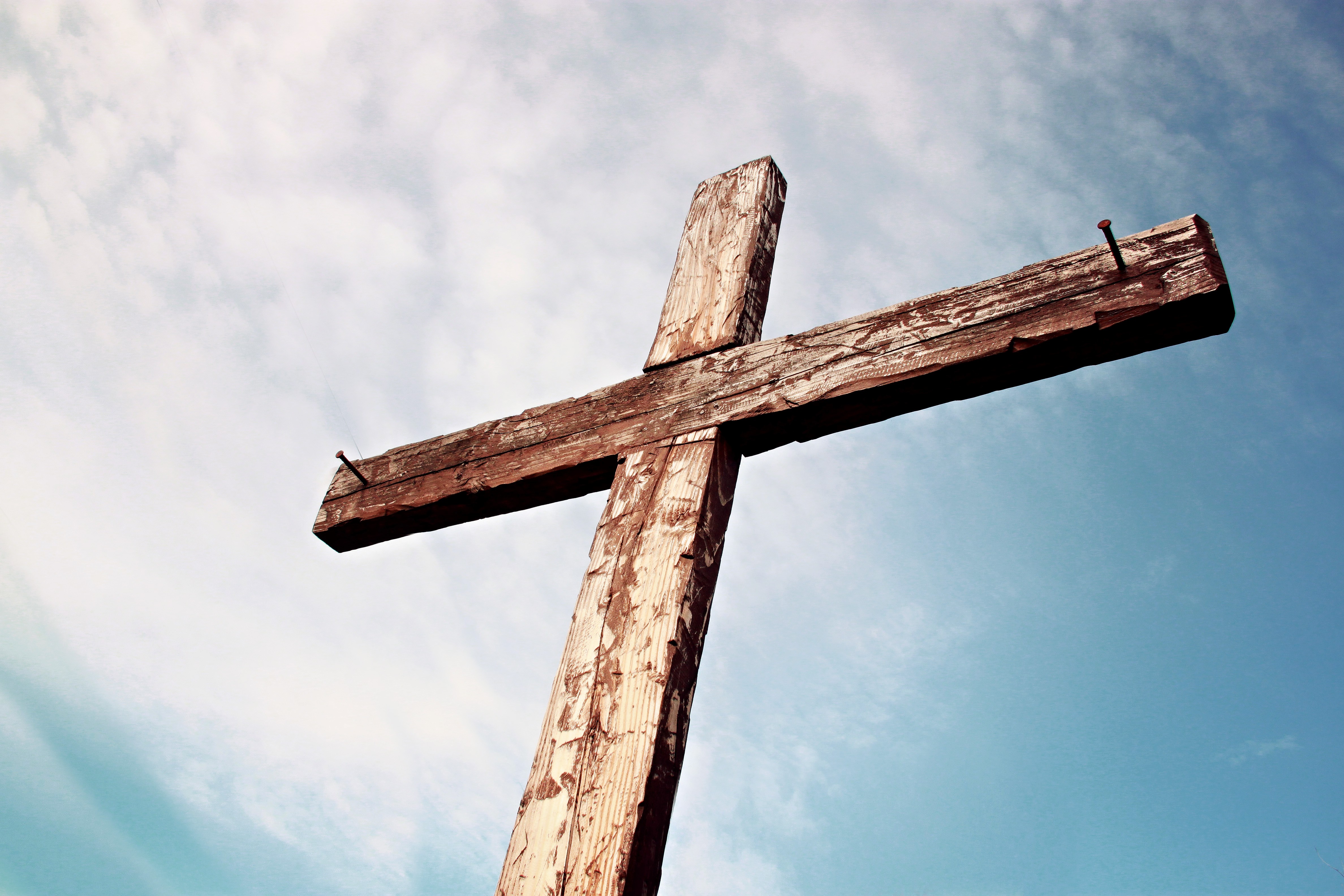 An old, rugged Christian cross set against a cloudy blue sky.