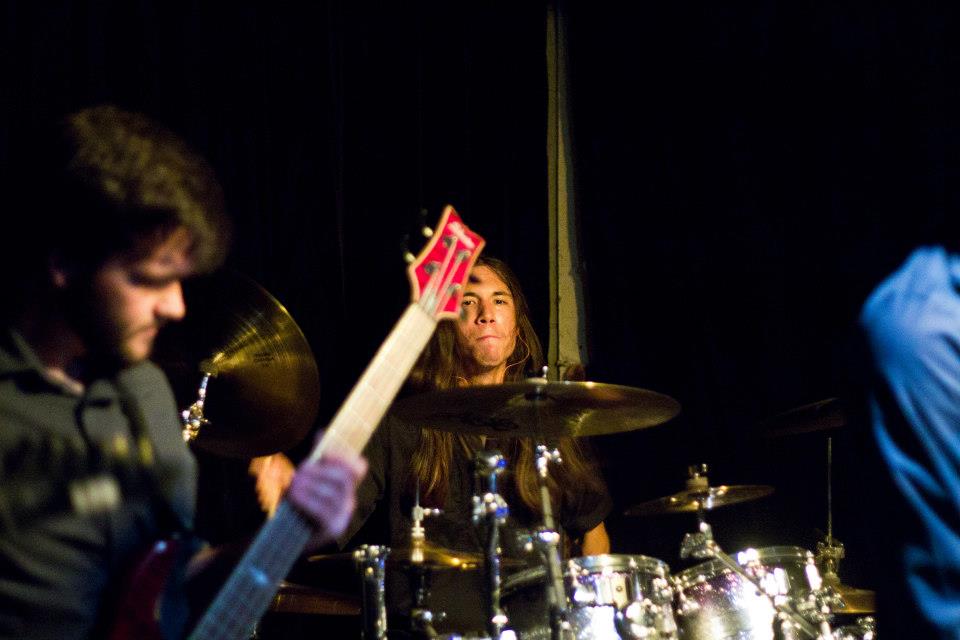 Eric Seal in the background of a live band playing, sitting behind his drums.